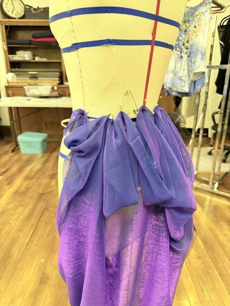 Computer with drafted pattern to be projected on to material future innovation and visionCONSTRUCTING THE PAPER FOR THE DESIGN PLANNING STEP 2 a picture of fabric waste why innovation and vision is important in custom dancewear future PROJECTING ON TO FABRIC CUSTOM PATTERN STEP 4 avatar-fit dancewear technology of fit -tech Start of one-of-a-kind Costume from Sewn 2 Dance draped on a mannequin this beautiful material of purple and navy blue and start of short cage that it is draped over.