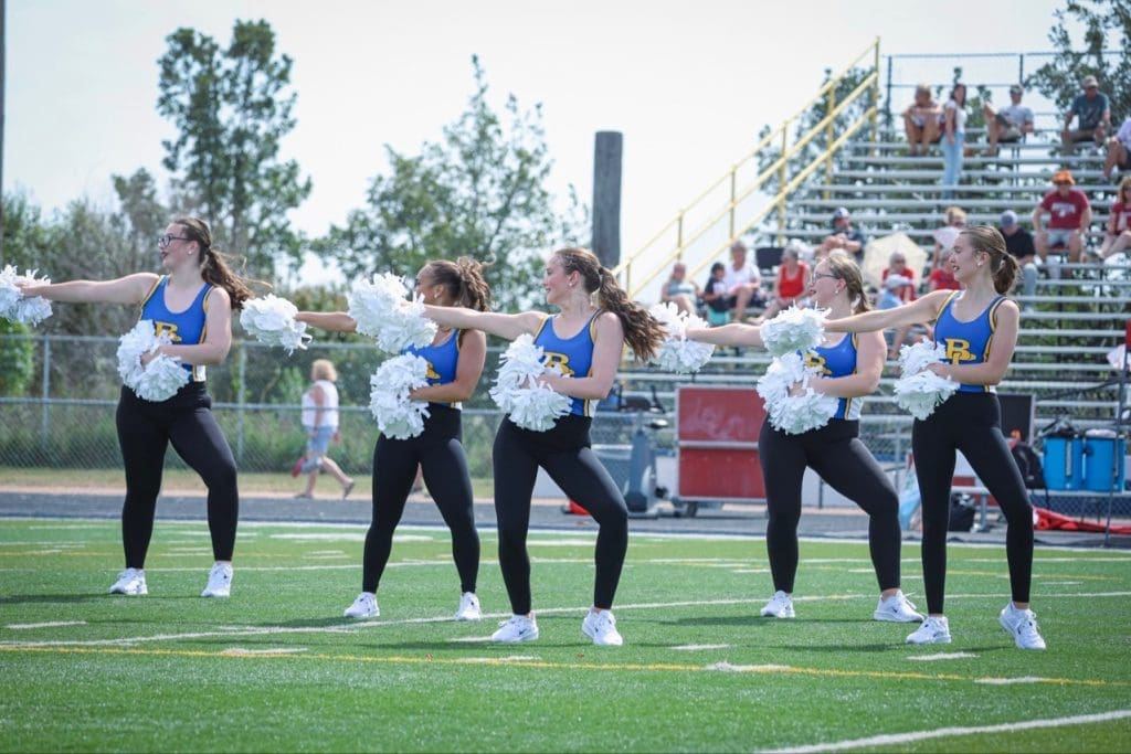 SOLO CUSTOM competetitve dancewear COSTUME CREATED BY SEWN 2 custom-fit dance costumes DANCE BLACK VELVET ONE SLEEVE WITH RUFFLE AND LARGE ROSE ON FRON Briar Cliff University in dance team in their custom game day costumes made by sewn 2 dance2025 performing on football field